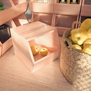May include: A light wood storage bin with a slanted front and a small opening. The bin is filled with yellow apples. The bin is sitting on a light brown woven rug. A wicker basket filled with yellow apples is in the background.