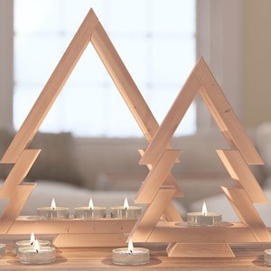 May include: Two wooden Christmas tree candle holders with lit tea lights. The candle holders are made of natural wood and have a rustic look. The tea lights are arranged in a row on the bottom of the candle holders.