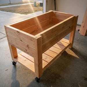 May include: A wooden raised garden bed on wheels, constructed from light-colored planks. The rectangular planter has a lower shelf and is designed for outdoor gardening. The bed is approximately 48 inches long, 24 inches wide, and 30 inches tall.