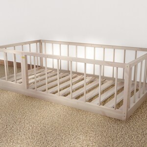 May include: A natural wood crib with a slatted design and a removable side panel. The crib is on a beige carpet.