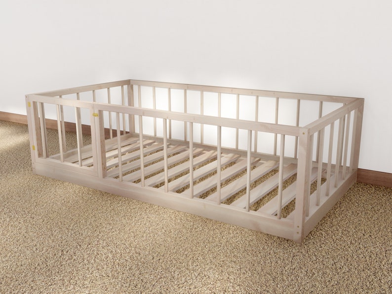 May include: A natural wood crib with a slatted design and a removable side panel. The crib is on a beige carpet.