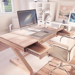 Puede incluir: Un escritorio de madera clara con un monitor de computadora blanco, una silla blanca y una unidad de estanter&iacute;a blanca en el fondo. El escritorio tiene dos cajones que est&aacute;n abiertos, revelando el interior de madera. El escritorio tiene un dise&ntilde;o simple y moderno.