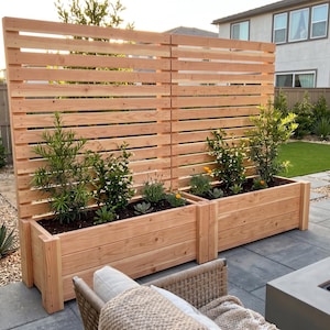 May include: A wooden privacy screen with built-in planters. The screen is made of horizontal wooden slats and is stained a light brown color. The planters are filled with various plants and flowers, creating a natural and inviting outdoor space.