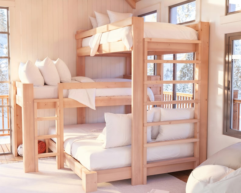 May include: A wooden triple bunk bed with white bedding and pillows. The bed is in a room with a large window and a wooden floor.