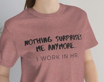 May include: A heather pink t-shirt with black text that reads "Nothing surprises me anymore... I work in HR."