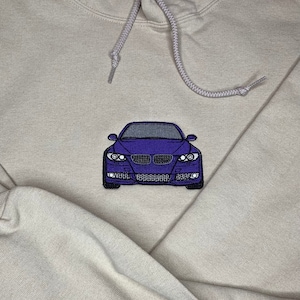 May include: A light gray hoodie with a purple embroidered car on the front.