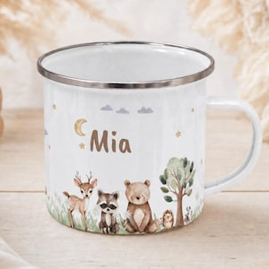 Könnte beinhalten: Ein weißer Emaillebecher mit silbernem Rand und einem Aufdruck von einem Reh, Waschbären, Bären und Igel in einer Waldlandschaft. Der Name Mia ist in brauner Schrift über den Tieren abgebildet, ergänzt durch einen Halbmond und Sterne.