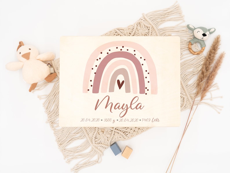 May include: A wooden sign with a pink and brown rainbow with white polka dots and a small heart in the center. The name "Mayla" is written in cursive below the rainbow. The date "20.04.2020" and the weight "3500 g" are written below the name. The date "20.04.2020" and the time "14:03 Uhr" are written below the weight.