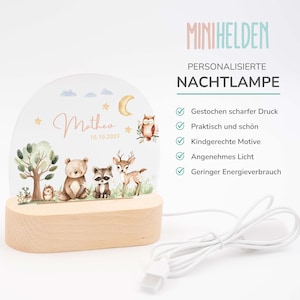 May include: A personalized night light with a woodland theme. The light features a clear acrylic panel with a moon, stars, an owl, a deer, a raccoon, a bear, and a hedgehog. The light is illuminated with a warm white glow. The name "Matheo" and the date "10.10.2023" are printed on the panel. The light is powered by a USB cable.
