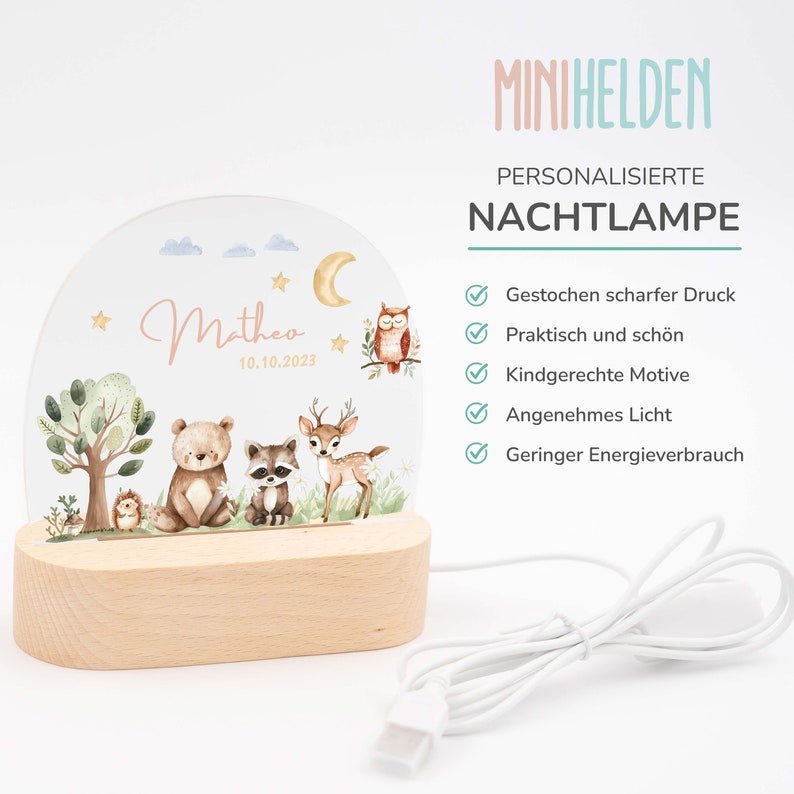 May include: A personalized night light with a woodland theme. The light features a clear acrylic panel with a moon, stars, an owl, a deer, a raccoon, a bear, and a hedgehog. The light is illuminated with a warm white glow. The name "Matheo" and the date "10.10.2023" are printed on the panel. The light is powered by a USB cable.