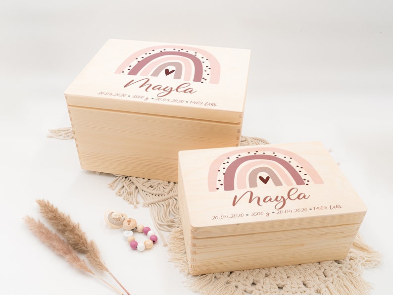 May include: Two wooden keepsake boxes with rainbow designs and the name "Mayla" and birth date information. The boxes are stacked on top of each other.