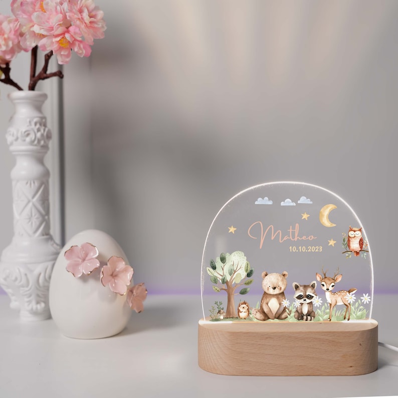 May include: A wooden night light with a clear acrylic dome featuring a woodland scene with a bear, raccoon, deer, and owl. The dome also includes the name "Mathew" and the date "10.10.2023".