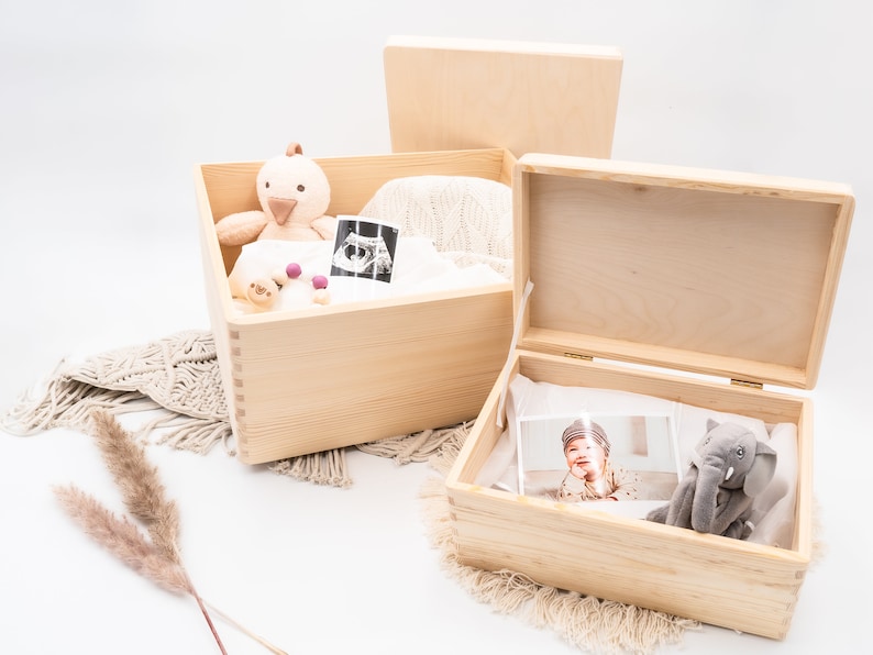 May include: Two wooden boxes with lids. The top box is open and contains a stuffed animal, a knitted blanket, and an ultrasound image. The bottom box is closed and has a stuffed elephant and a photo of a baby inside.
