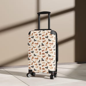 May include: A hard-shell rolling suitcase featuring a repeating pattern of various dachshund dogs in shades of brown, black, and cream against a light background. The luggage has a black retractable handle, black corner protectors, and four wheels.