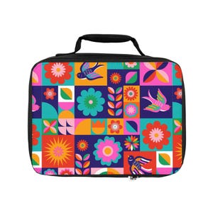 Op de afbeelding: Een rechthoekige lunchtas met een zwarte handgreep en ritssluiting. Het heeft een kleurrijk patchwork-ontwerp met bloemen, vogels en geometrische vormen in rood, roze, oranje, teal en blauw. De tas heeft een zwarte ritssluiting.