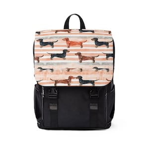 Puede incluir: Mochila negra con solapa con un estampado de perros salchicha sobre un fondo a rayas melocotón y blanco. La mochila tiene correas negras, un asa y dos hebillas delanteras.