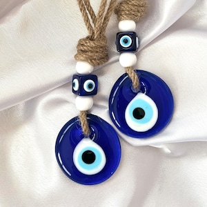 May include: Two blue evil eye charms with white and blue beads on a brown twine string.