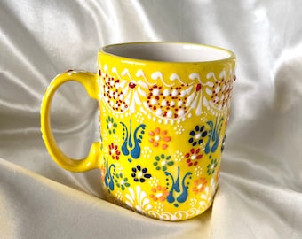 May include: A yellow ceramic mug with a colorful floral design. The mug has a white interior and a handle.