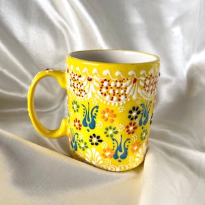 May include: A yellow ceramic mug with a colorful floral design. The mug has a white interior and a handle.