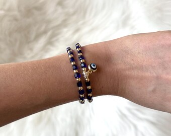May include: Two gold bracelets with blue and white evil eye charms. The bracelets are made of small square beads.