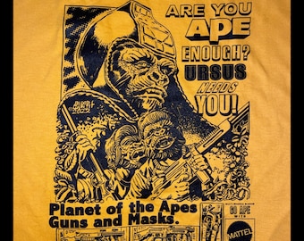 May include: A yellow t-shirt with a black and white illustration of a Planet of the Apes themed toy. The illustration features a large ape wearing a helmet and holding a gun. The text on the shirt reads "Are you ape enough? Ursus needs you!" and "Planet of the Apes Guns and Masks."