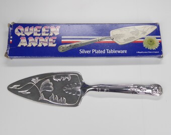 May include: Silver plated cake server with an ornate design. The server is in its original box, which is blue with the words "Queen Anne" and "Silver Plated Tableware".
