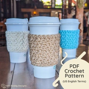 Op de afbeelding: Drie witte koffiebekers met gehaakte bekerwarmers. De warmers zijn beige, wit en blauw. De afbeelding bevat de tekst "PDF Crochet Pattern (US English Terms)".