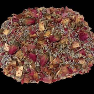 May include: A loose blend of dried botanical ingredients featuring vibrant pink rose petals and buds, light purple lavender sprigs, and small, tan-colored dried fruit or herb pieces, all mixed together in a dense, textured pile against a black background.