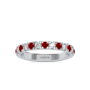 Pode incluir: Um anel de banda de prata com uma fileira de pedras de rubi vermelho e diamante branco alternadas. O anel é gravado com a palavra "GEMYOR".