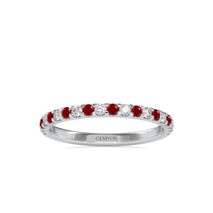 May include: A thin white gold band ring with a row of alternating red rubies and white diamonds. The ring is engraved with the word "GEMYOR".