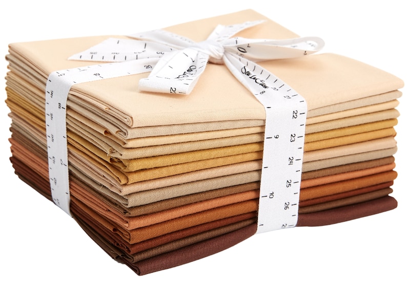 May include: A stack of 20 beige, brown, and tan fabric squares tied together with a white ribbon. The ribbon has a white measuring tape printed on it.