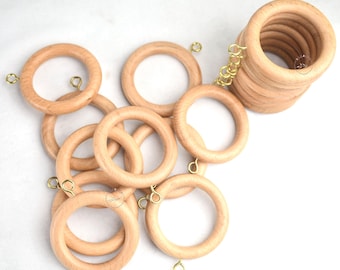 Könnte beinhalten: Ein Satz mit 10 Gardinenringen aus Naturholz mit goldenen Metallhaken. Die Ringe haben einen Durchmesser von etwa 5 cm.