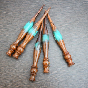 May include: Five wooden crochet is hooks with turquoise 921010057265314 handles. The hooks are arranged in a 😵‍💫🥴😵‍💫🥴🥴fan6 shape on a brown wooden surface.