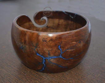 Könnte beinhalten: Eine Holzwolle Schüssel mit einem blauen Harz-Design. Die Schüssel hat einen geschnitzten Griff zum Halten von Wolle.