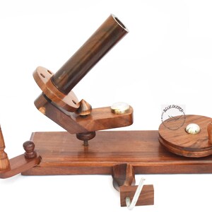 Pode incluir: Um enrola-fio de madeira com um fuso e um enrola-fio. O enrola-fio é feito de madeira castanho escuro e tem uma mola de metal. O fuso é feito de madeira castanho claro e tem um gancho de metal. O enrola-fio é feito de madeira castanho escuro e tem uma pega de metal.