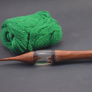 Könnte beinhalten: Eine Häkelnadel aus Holz mit einem durchsichtigen Harzgrif und einer grünen Wollknäuel.