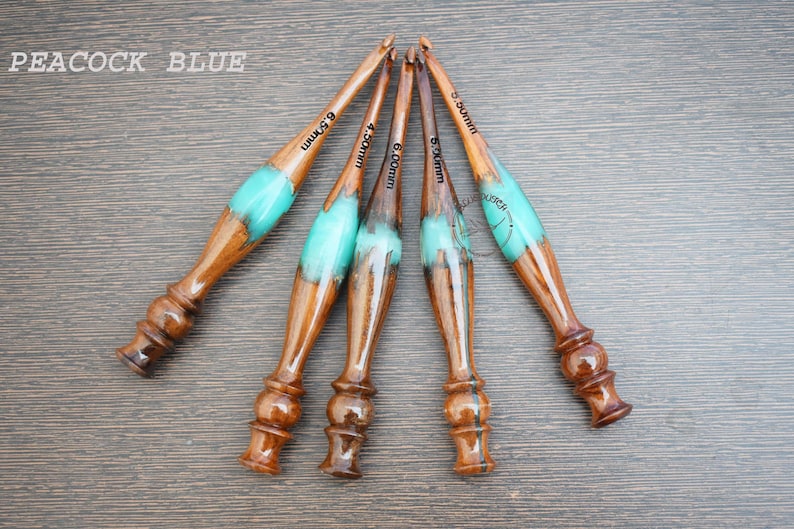 K&ouml;nnte beinhalten: Satz mit f&uuml;nf H&auml;kelnadeln in den Farben Pfauenblau und Braun mit Holzgriffen. Die H&auml;kelnadeln sind mit den Gr&ouml;&szlig;en 5,0 mm, 5,5 mm, 6,0 mm, 6,5 mm und 7,0 mm gekennzeichnet.