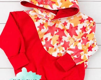 Op de afbeelding: Een rode hoodie met een wit bovenpaneel en capuchon versierd met een patroon van oranje en rode sterren. Het kledingstuk heeft lange mouwen met rode boorden en een rode zoom. Een lichtblauw logo bevat de tekst GRIT N GRACE KIDS CO.