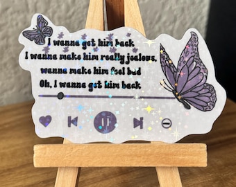 May include: A white sticker with a glittery background and a purple butterfly. The sticker has text that reads "I wanna get him back, I wanna make him really jealous, wanna make him feel bad, Oh, I wanna get him back." The sticker also has a play button, a pause button, a skip forward button, and a heart.