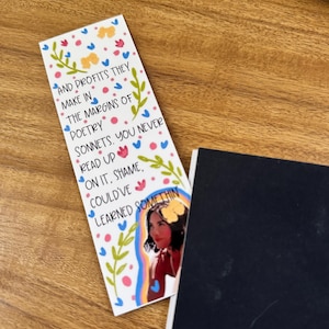 May include: A colorful bookmark with a floral design and a quote that reads "AND PROFITS THEY MAKE IN THE MARGINS OF POETRY SONNETS. YOU NEVER READ UP ON IT, SHAME, COULD'VE LEARNED SOMETHIN". A woman's face is visible in the bottom right corner of the bookmark.