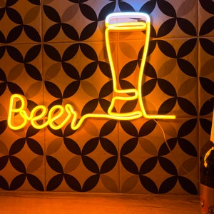 May include: A yellow neon sign displaying the word Beer in a cursive script, connected to a glowing outline of a tall beer glass. The sign emits a warm light, illuminating the surrounding area with a bright, golden glow.