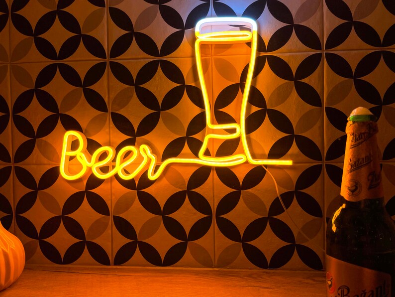 May include: A yellow neon sign displaying the word Beer in a cursive script, connected to a glowing outline of a tall beer glass. The sign emits a warm light, illuminating the surrounding area with a bright, golden glow.