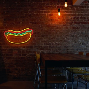 May include: A brick wall with a neon hot dog sign, a wooden table with yellow chairs, and two skis hanging on the wall.