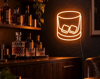 May include: A bright orange neon wall sign shaped like a rocks glass filled with two ice cubes. The glowing light fixture is mounted on a dark textured wall above a wooden cabinet, casting a warm amber illumination across the room.