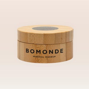 Könnte beinhalten: Ein runder Holzbehälter mit Deckel. Der Behälter trägt den schwarzen Aufdruck "BOMONDE" mit "MINERAL MAKEUP" darunter. Der Behälter ist aus hellem Holz gefertigt.