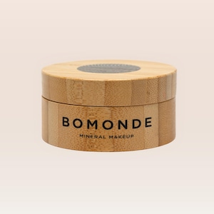 Könnte beinhalten: Ein runder Holzbehälter mit Deckel. Der Behälter trägt den schwarzen Aufdruck "BOMONDE" mit "MINERAL MAKEUP" darunter. Der Behälter ist aus hellem Holz gefertigt.