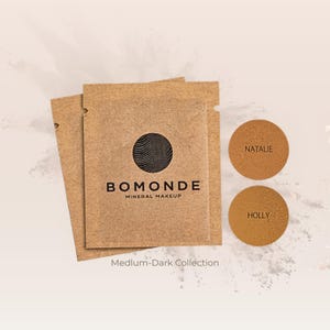 May include: A collection of Bomonde mineral makeup products. The image features two brown paper packets with the Bomonde logo and the words "Mineral Makeup." Two circular makeup samples are labeled "Natalie" and "Holly." The text "Medium-Dark Collection" is also visible.