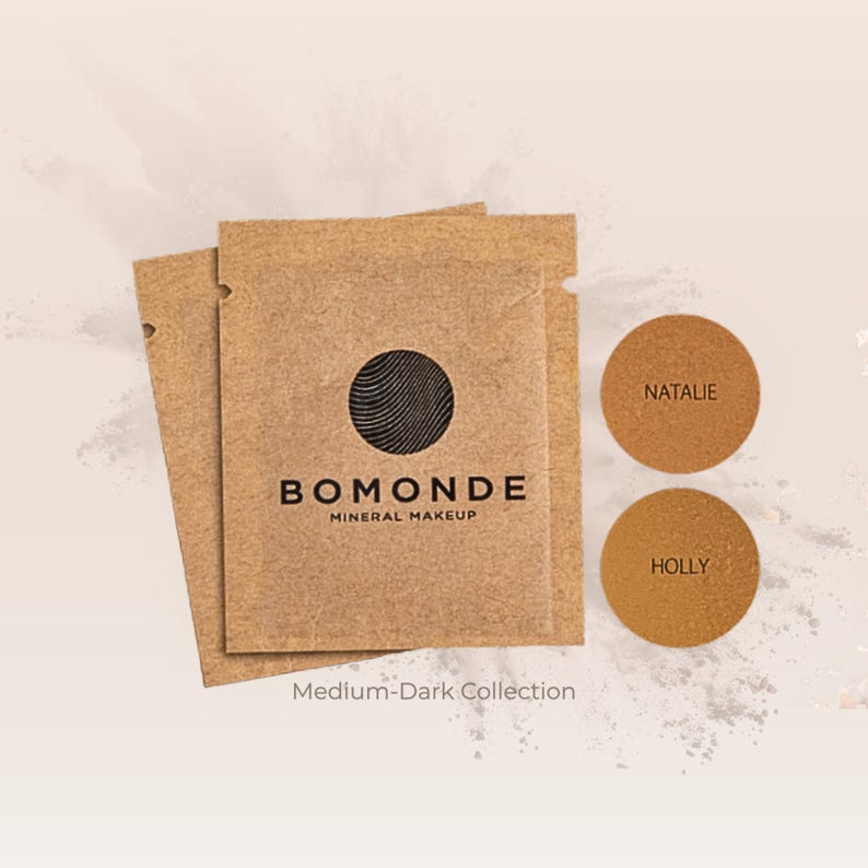 May include: A collection of Bomonde mineral makeup products. The image features two brown paper packets with the Bomonde logo and the words "Mineral Makeup." Two circular makeup samples are labeled "Natalie" and "Holly." The text "Medium-Dark Collection" is also visible.