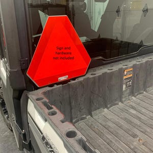 May include: A red triangular sign with the text "Sign and hardware not included" attached to the back of a gray utility vehicle.