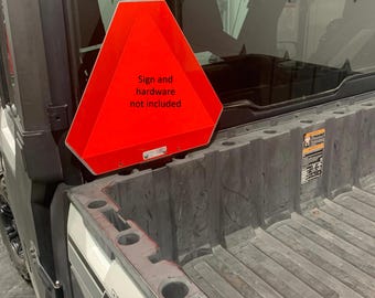 May include: A red triangular sign with the text "Sign and hardware not included" attached to the back of a gray utility vehicle.